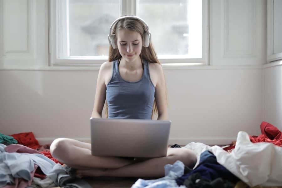 Woman listening to podcasts while working on laptop on bed