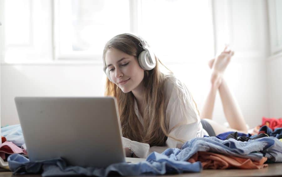 woman working on laptop and listening to podcast on bed